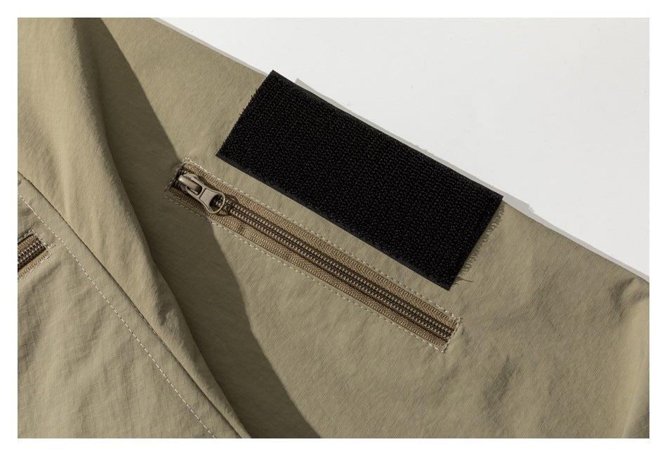 Close-up of a khaki jacket sleeve with a zipper pocket and black hook-and-loop cuff tab.