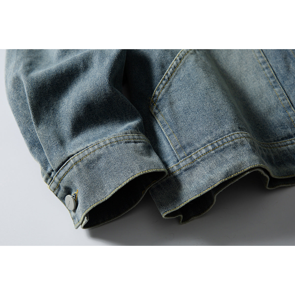 Close-up of the faded blue denim jacket's buttoned cuff and stitched sleeve hem.