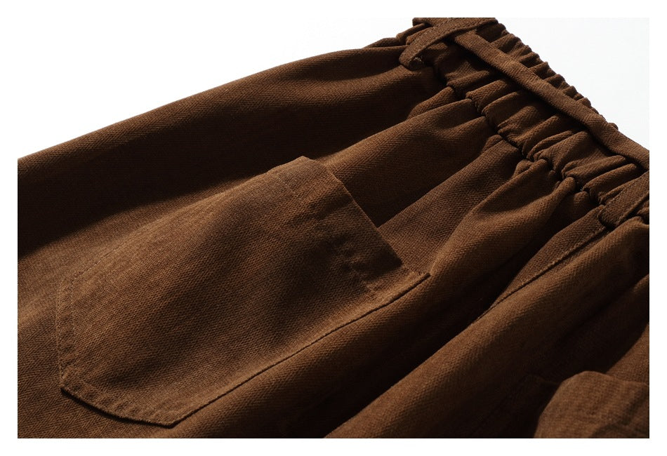 Close-up of brown trousers showing a stitched patch pocket and gathered elastic waistband.