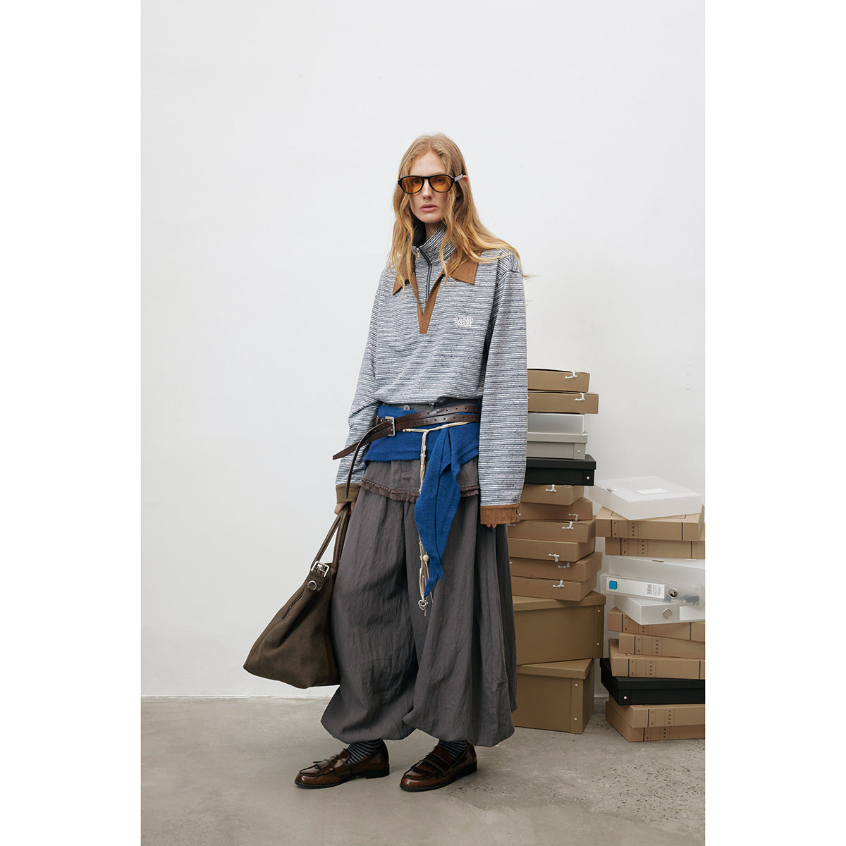 Full-length view of a woman wearing a gray striped pullover with a brown collar, styled with a long skirt and blue wrap.