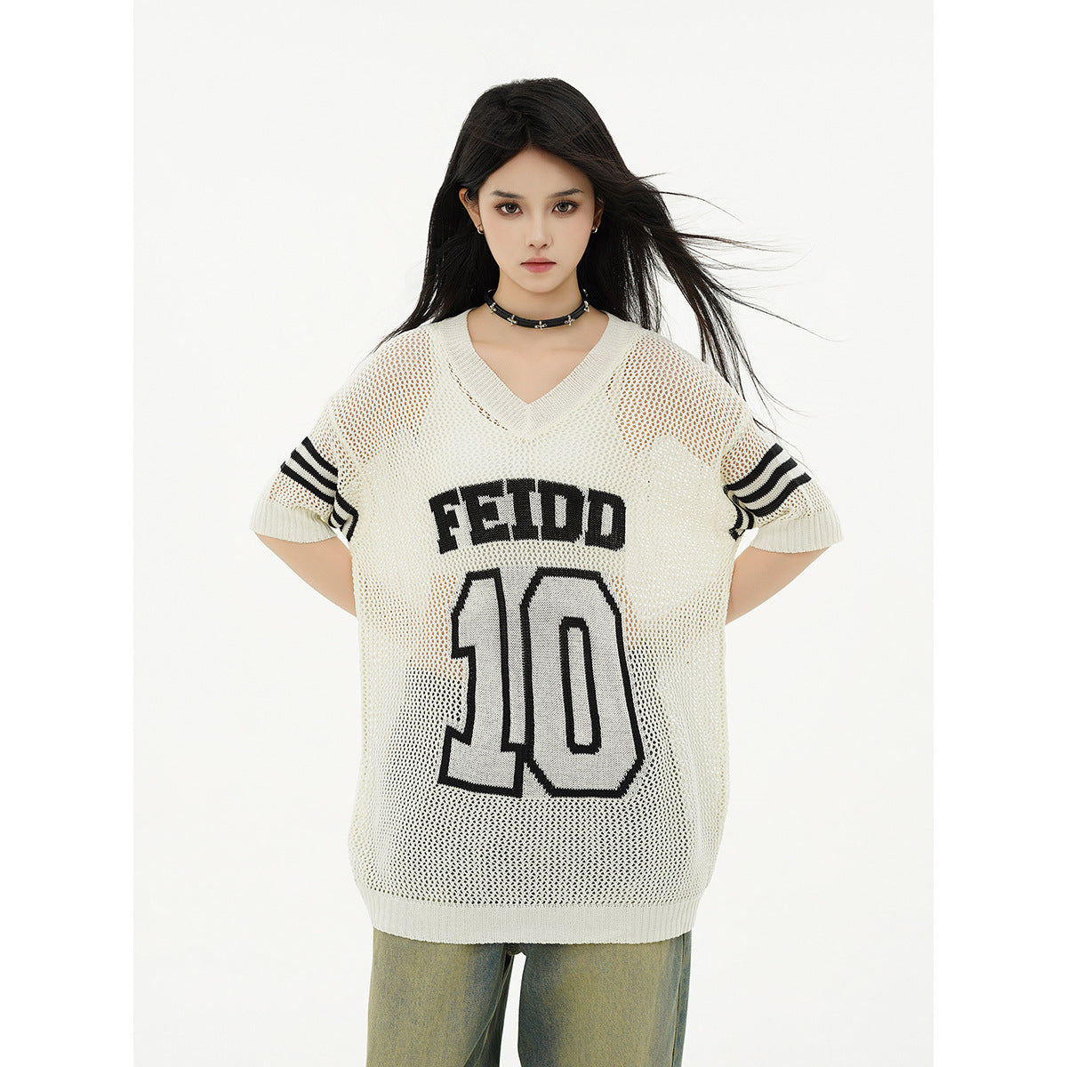 Close front view of a model in an ivory mesh V-neck tunic with black sleeve stripes and bold FEIDD 10 lettering.