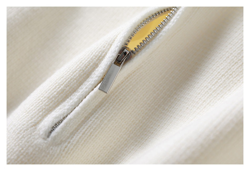 Close-up of a silver zipper set into the ivory knit fabric of a sweater.