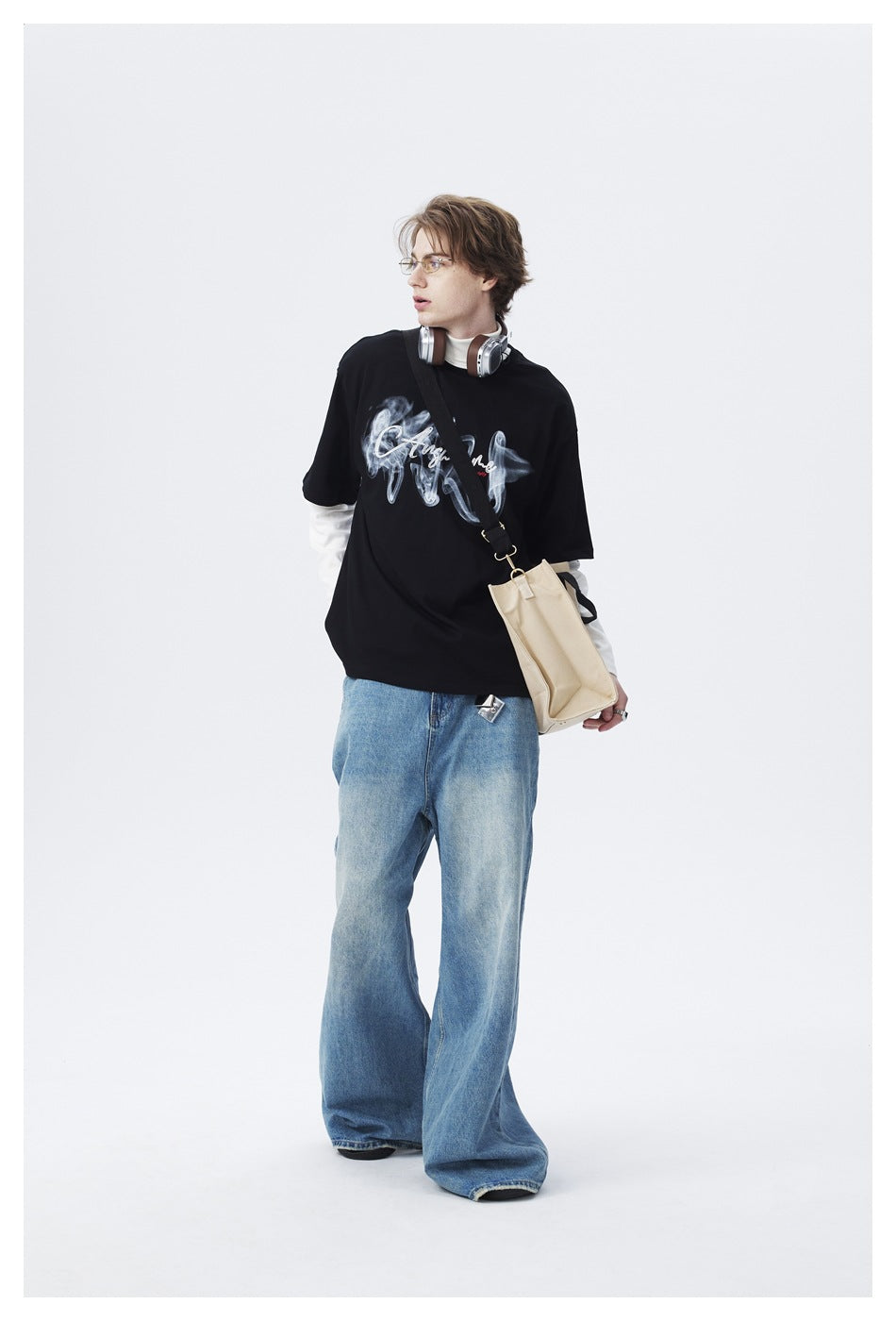 Model wearing a black graphic T-shirt layered over white sleeves with wide-leg light-blue jeans.