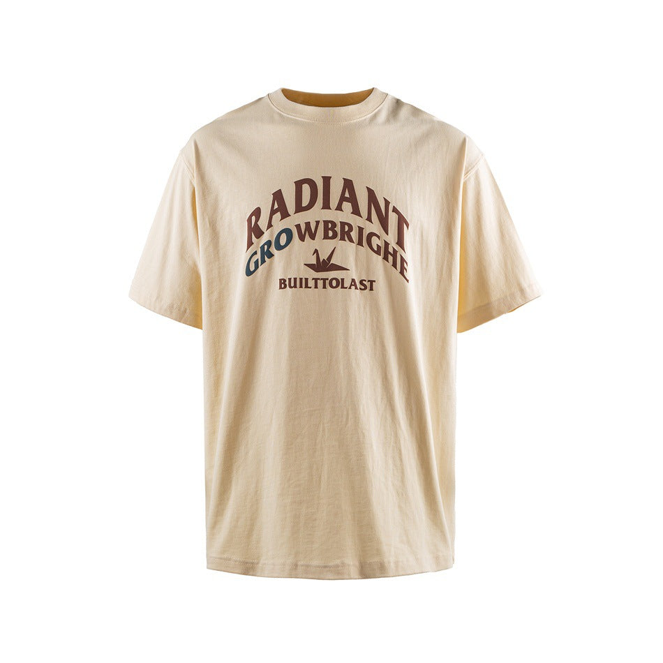 Cream short-sleeve T-shirt with arched brown and green lettering and a small graphic on the chest.