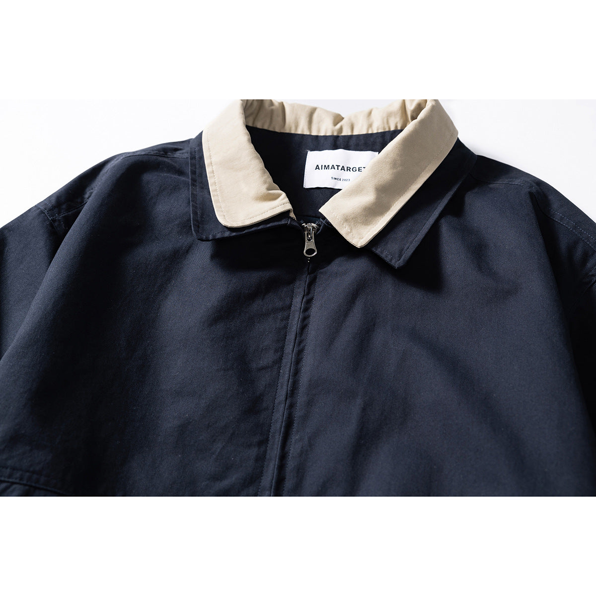 Close-up of a navy jacket with a contrasting beige collar, front zipper, and sewn neck label.