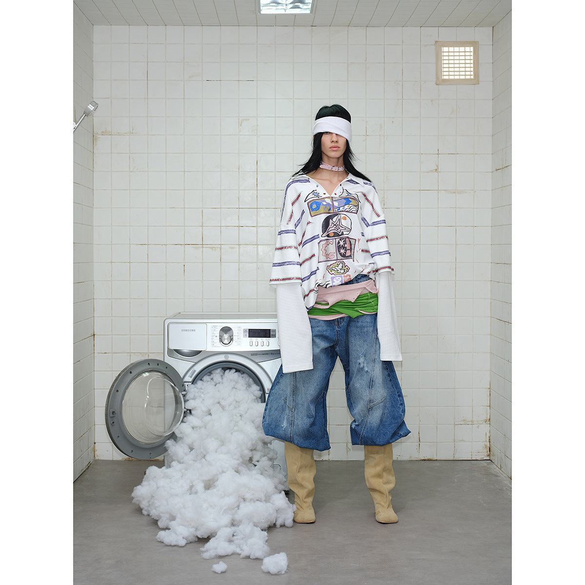 Full-length model wearing an oversized white graphic polo with multicolor stripes, wide cropped jeans, and tan boots.