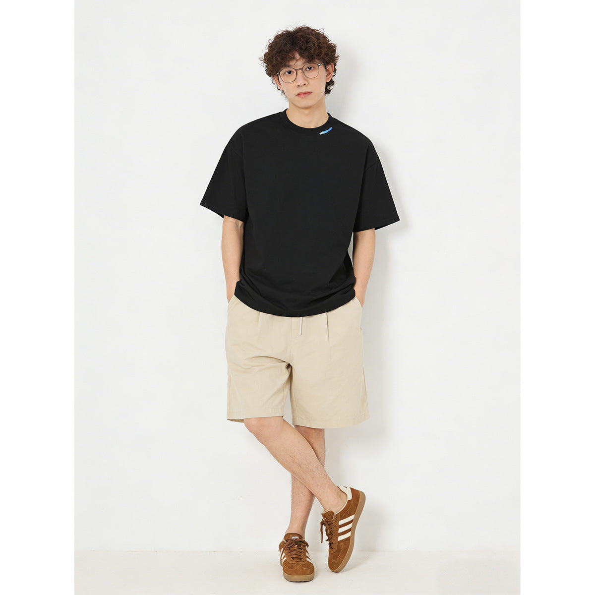 Model wearing an oversized black short-sleeve T-shirt with a small blue neckline detail and light beige shorts.