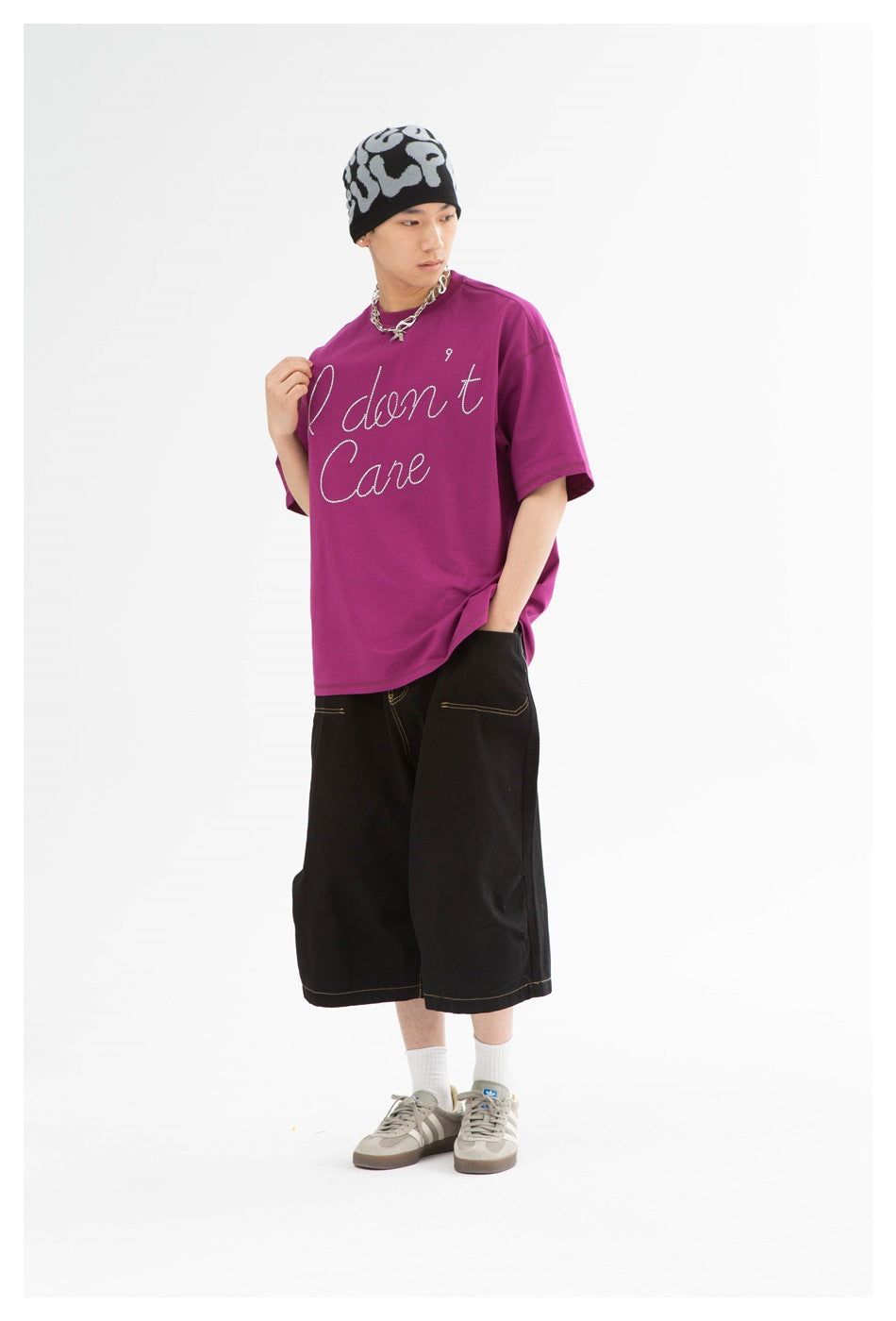 Model wearing a purple short-sleeve T-shirt with script rhinestone-dot lettering, black wide shorts and gray sneakers