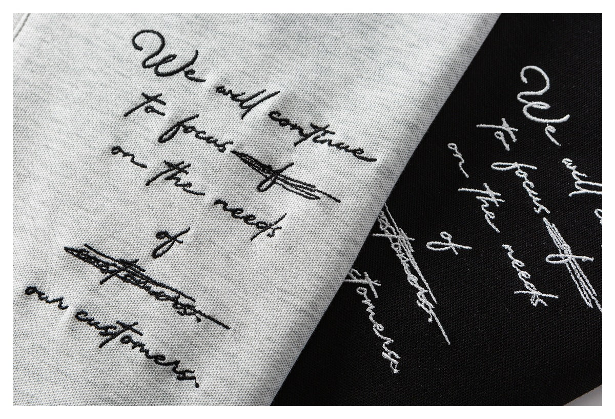 Close-up of cursive text and crossed-out marks printed on light gray and black shirt fabric.