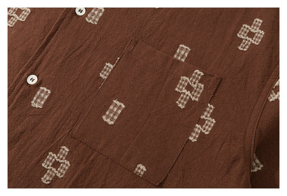 Close-up of a brown garment showing a chest pocket, white buttons, and cream geometric motifs.