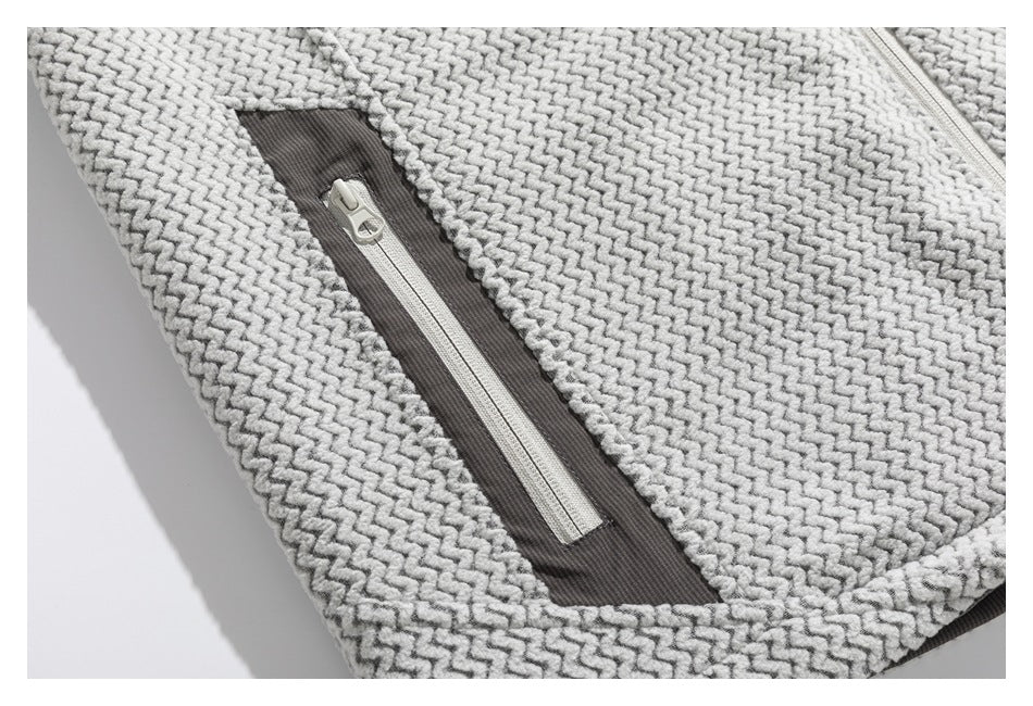 Close-up of a light gray patterned jacket with a vertical zip pocket set in a dark gray panel.
