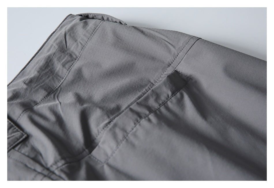Close-up of gray trousers showing the waistband, stitching, and pocket seam.