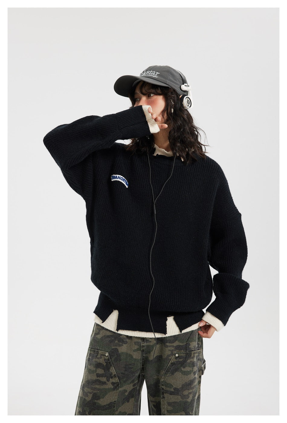 Front view of a model in a black ribbed sweater with cream collar, cuffs, and hem, styled with camouflage pants.