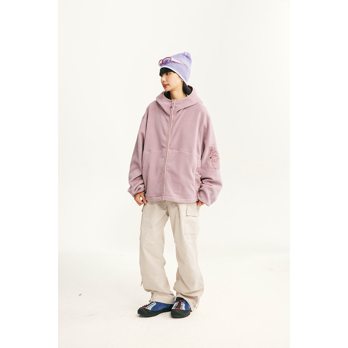 Model wearing a dusty pink hooded zip-up jacket with a sleeve pocket and light cargo pants.
