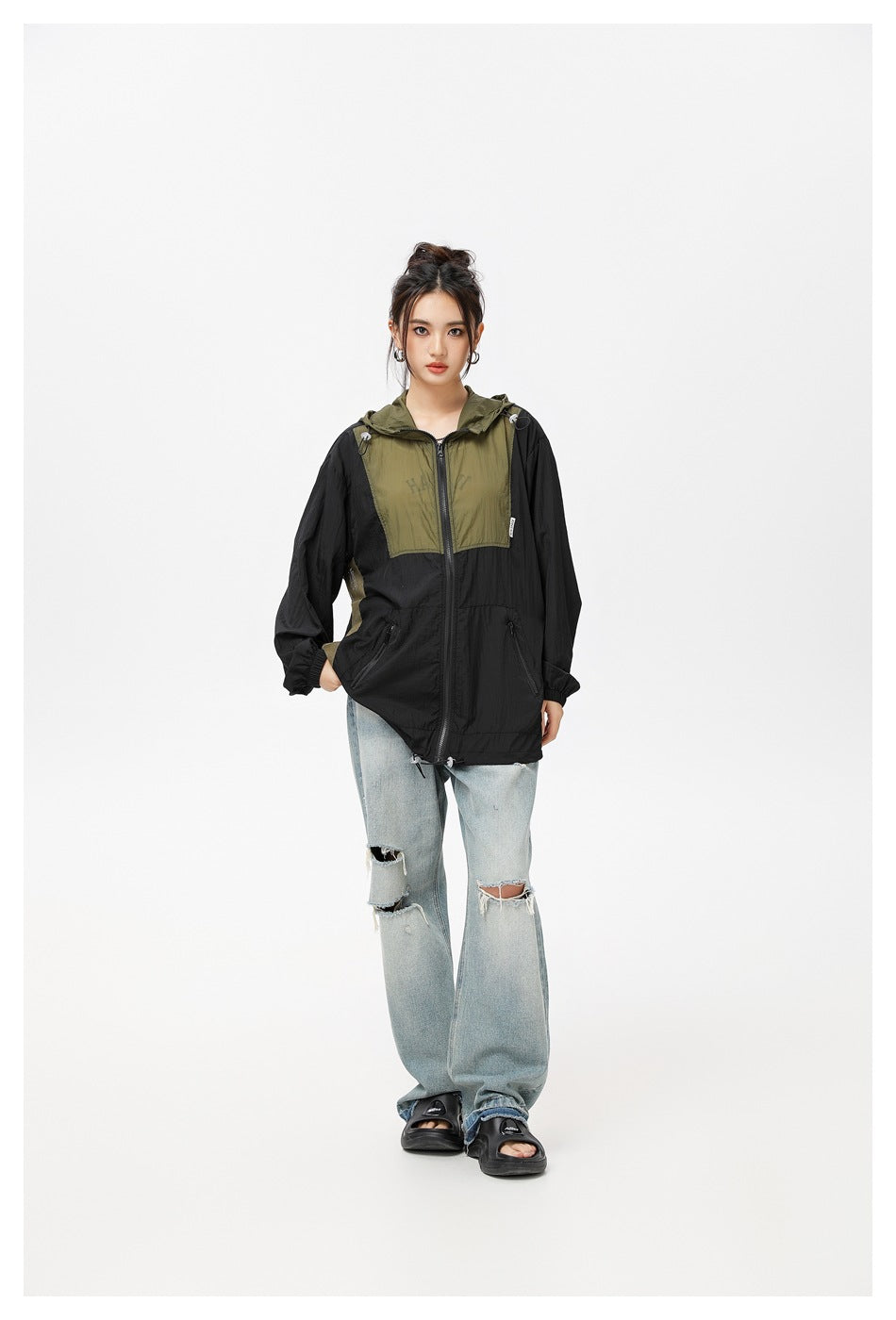 Model wearing a black and olive hooded zip jacket with ripped light-wash jeans and black sandals, front view