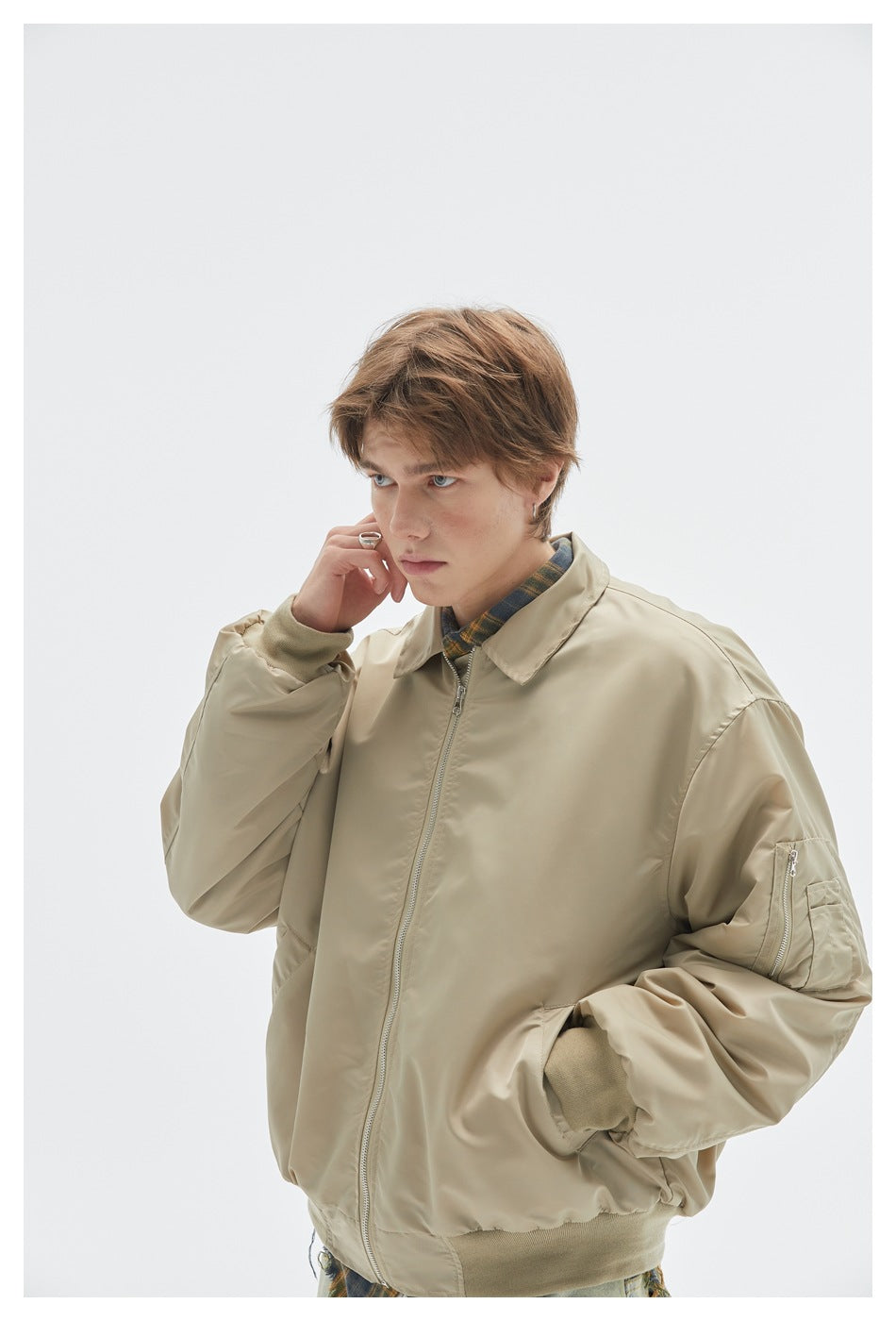 Model in a close view of a beige bomber jacket with a front zipper, ribbed cuffs and hem, and a sleeve pocket.
