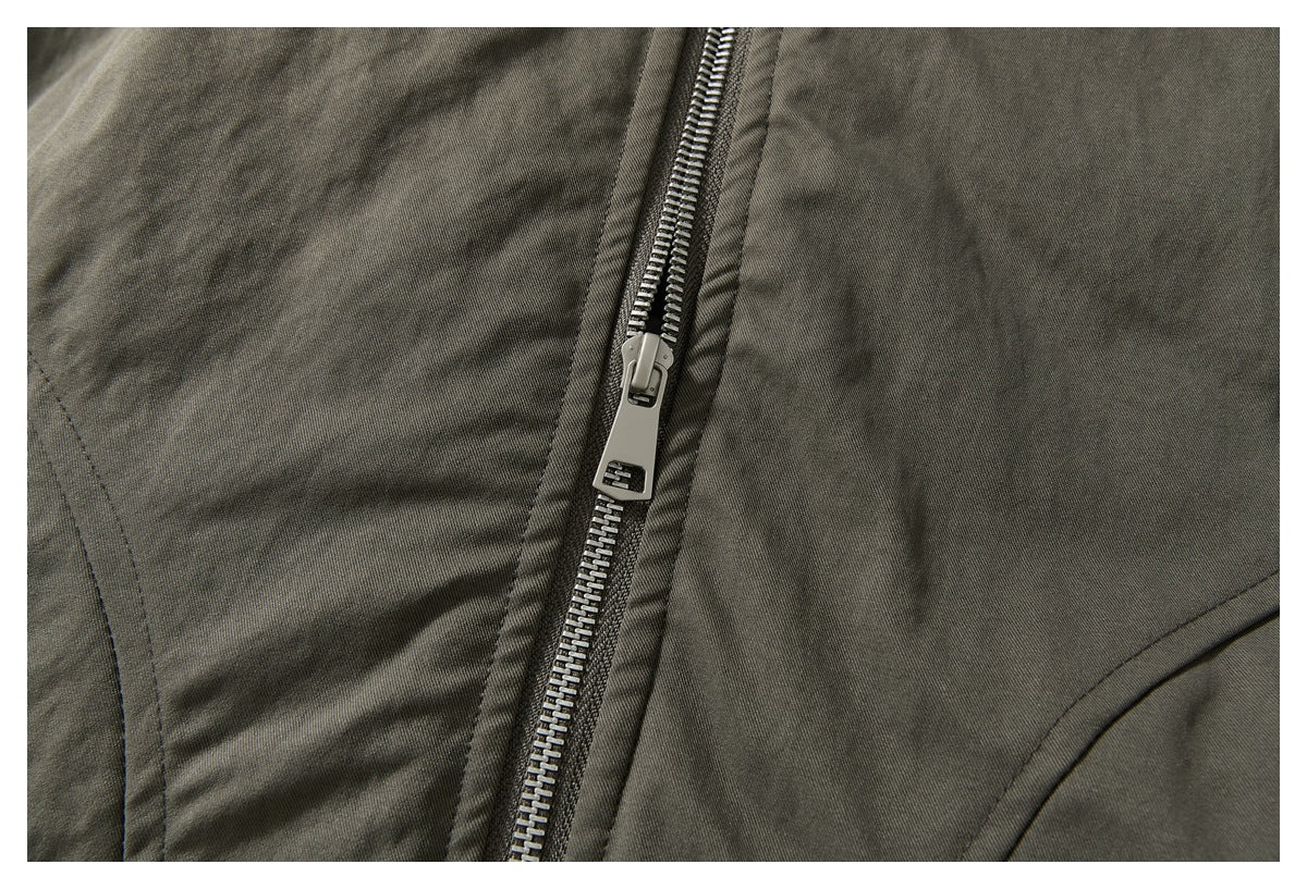 Close-up of an olive-gray garment with a prominent metal zipper and curved stitched seams.