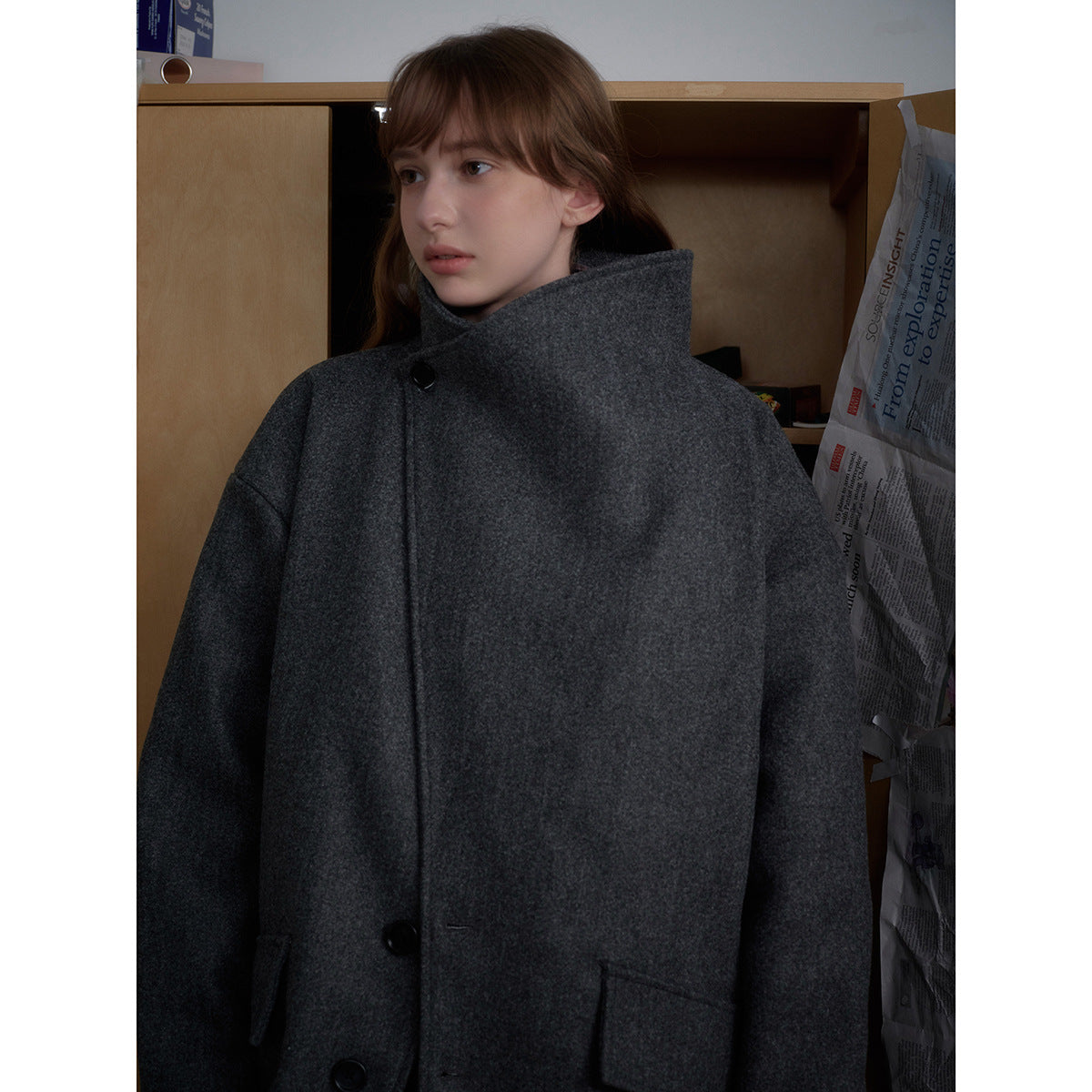 Close view of a woman wearing a charcoal-gray coat with a high stand collar and large dark buttons.