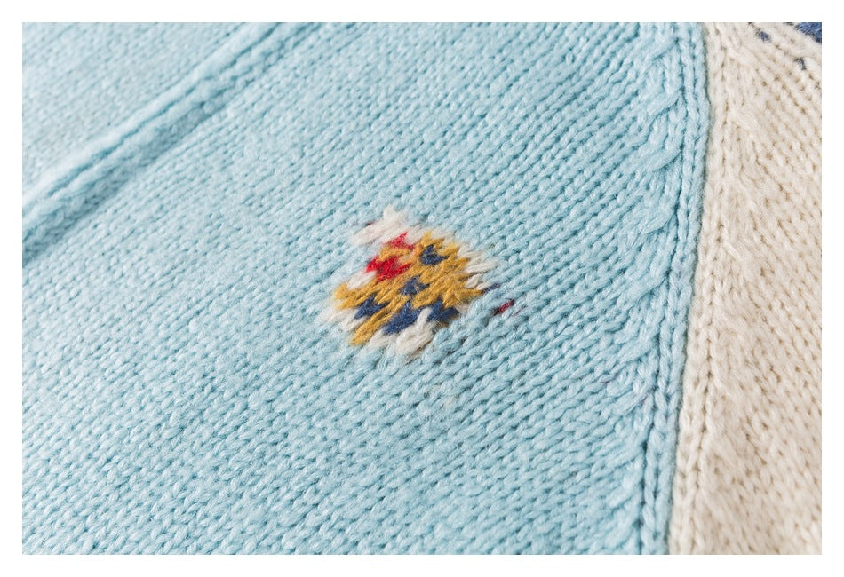 Close-up of a small red, yellow, blue, and cream embroidered motif on aqua knit fabric.