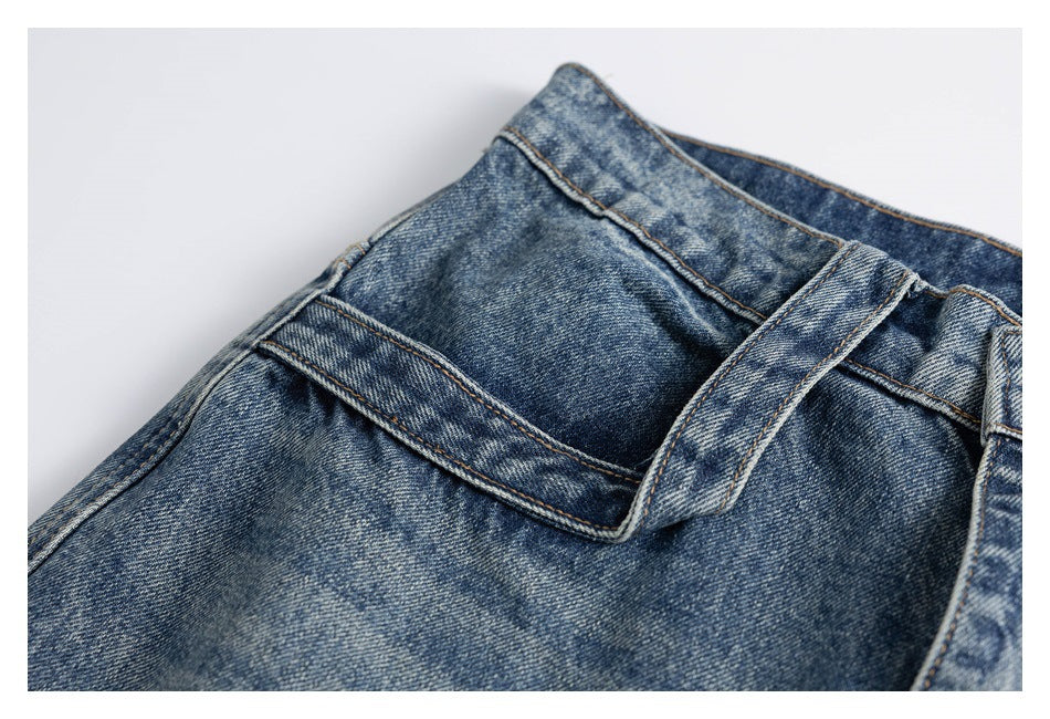 Close-up of blue washed jeans showing the waistband, belt loop, stitching, and front pocket area.
