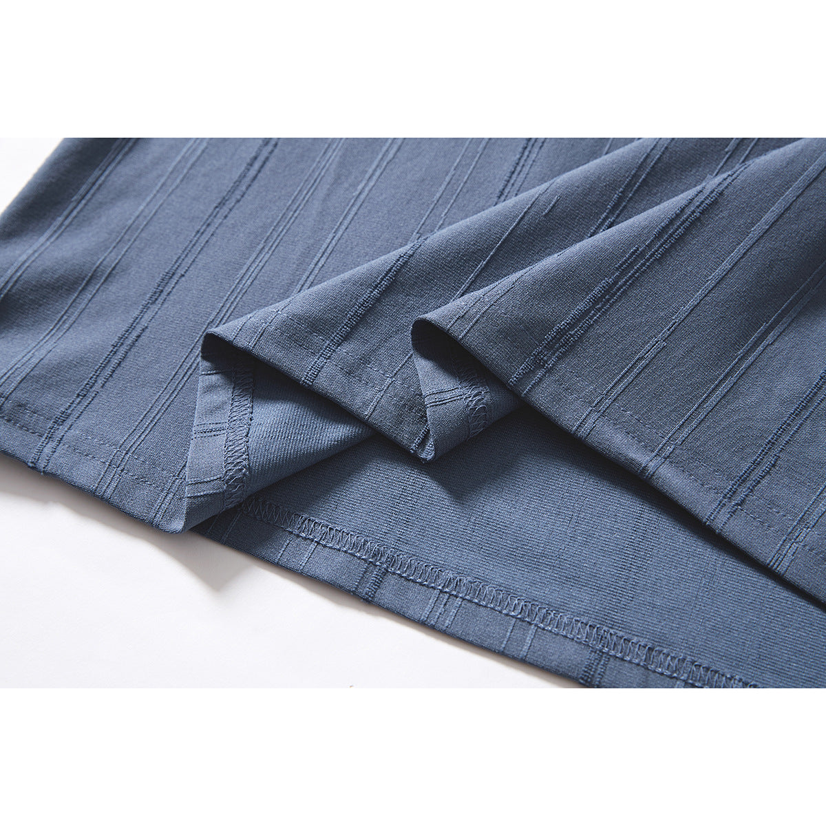 Close-up of the blue T-shirt hem, turned up to show stitching and the vertical stripe pattern.