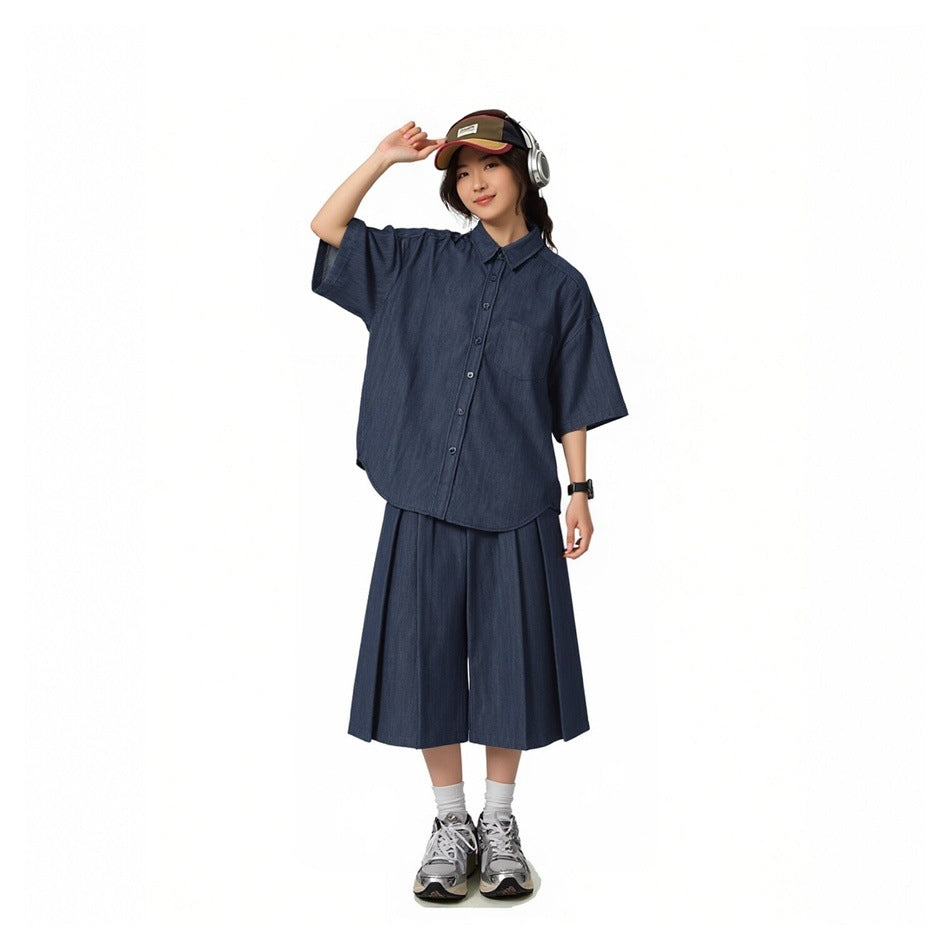 Model wearing a blue short-sleeve button-up shirt with matching pleated wide-leg shorts, cap and sneakers