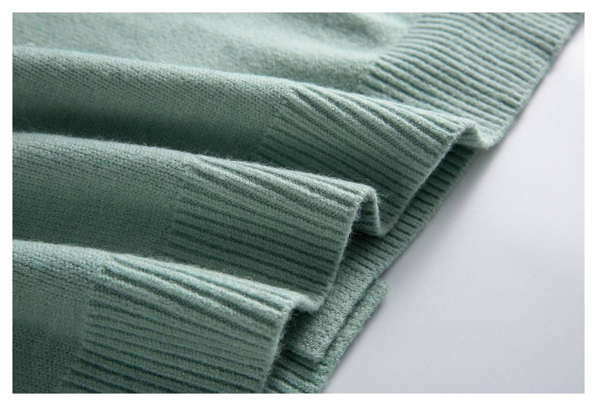 Close-up of pale sage-green sweater sleeves with ribbed cuffs and a ribbed hem.