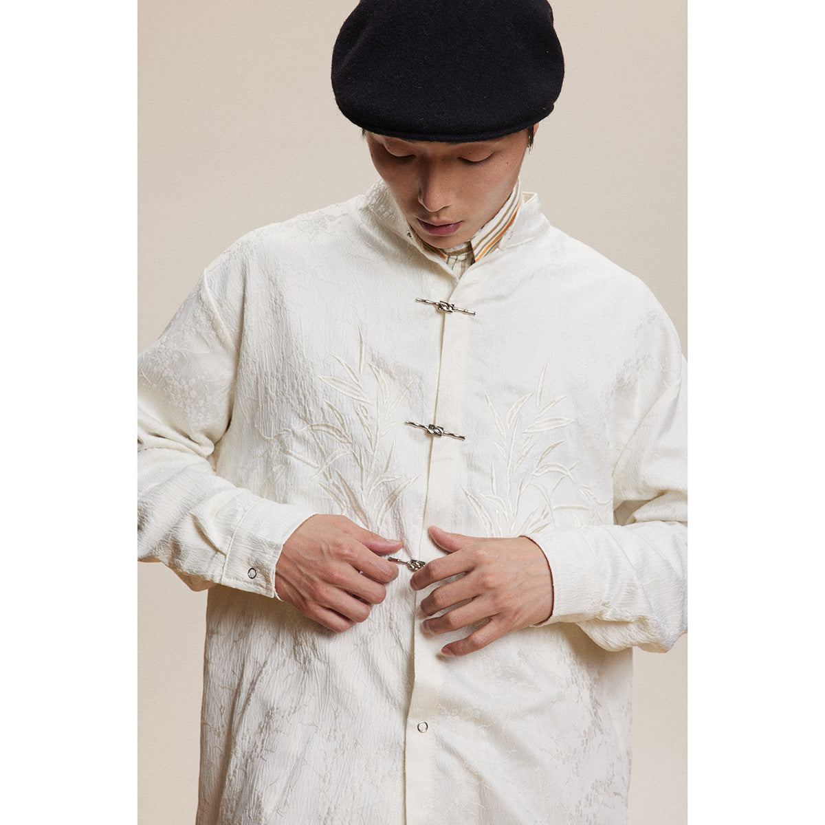 Close view of a model wearing an ivory jacket with raised bamboo embroidery and metal frog closures.