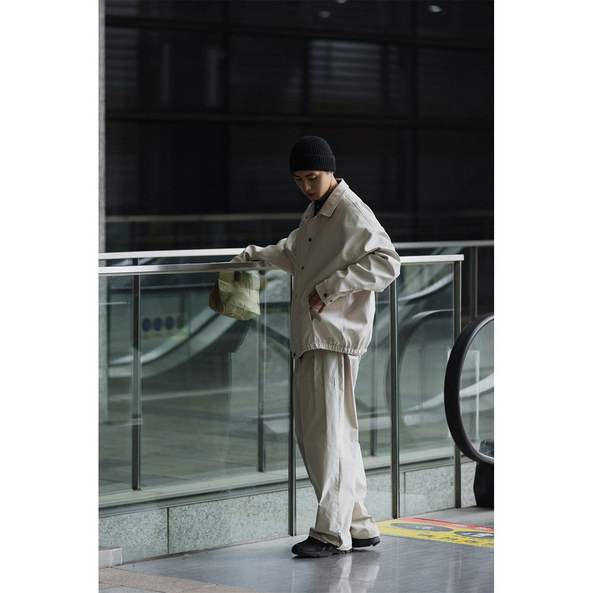 Model in a light beige oversized jacket and matching trousers beside a glass railing.