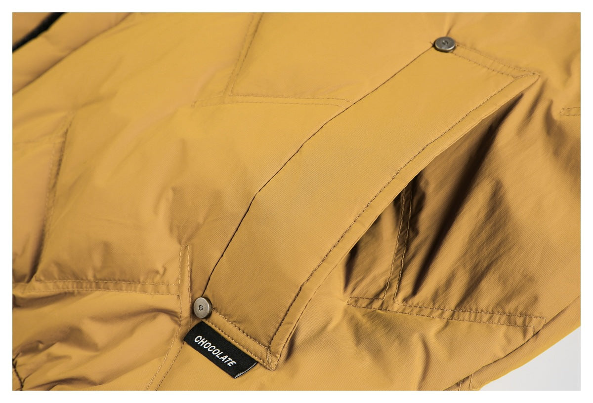 Mustard garment close-up showing a buttoned flap pocket and a small black CHOCOLATE label.