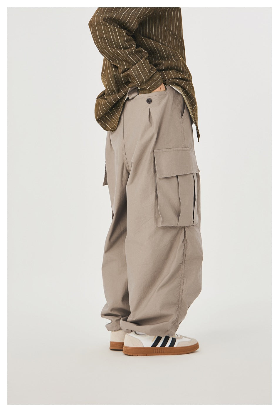 Rear-side view of a model wearing loose taupe cargo pants with a large flap cargo pocket.