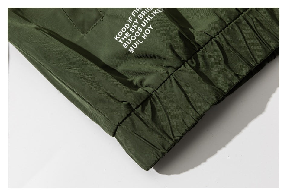 Close-up of a dark olive jacket's gathered elastic hem with partial white printed text.