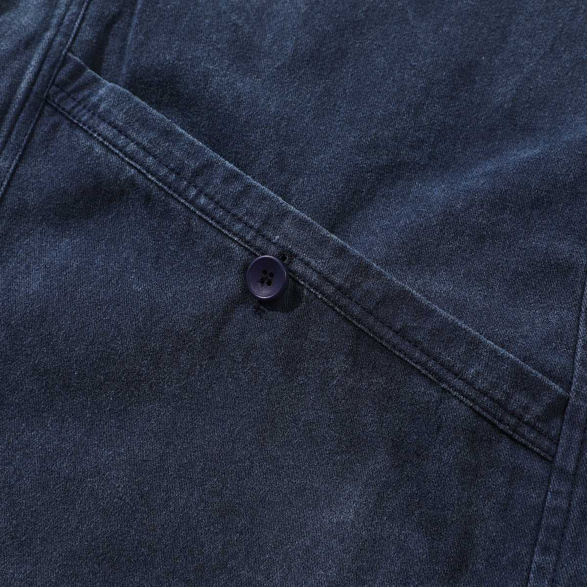 Close-up of dark indigo garment fabric with a diagonal stitched seam and a dark four-hole button.