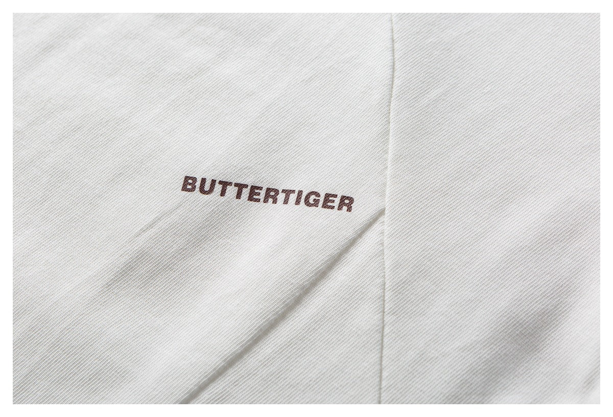 Close-up of white garment fabric with a dark “BUTTERTIGER” print and a nearby seam.