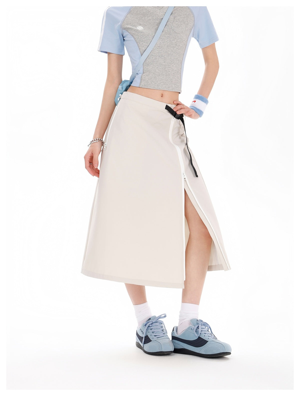 Model wearing an ivory midi skirt with a side zipper opened into a slit and a black belt detail, paired with a gray and blue
