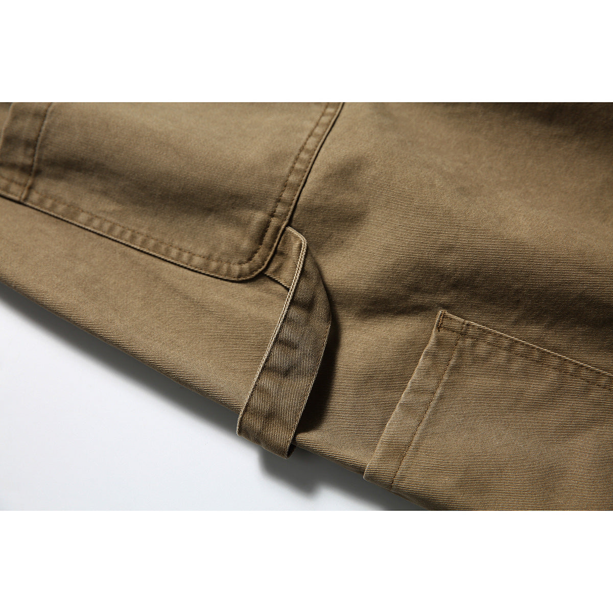 Close-up of tan utility pants showing a pocket edge, stitching, and a fabric loop.