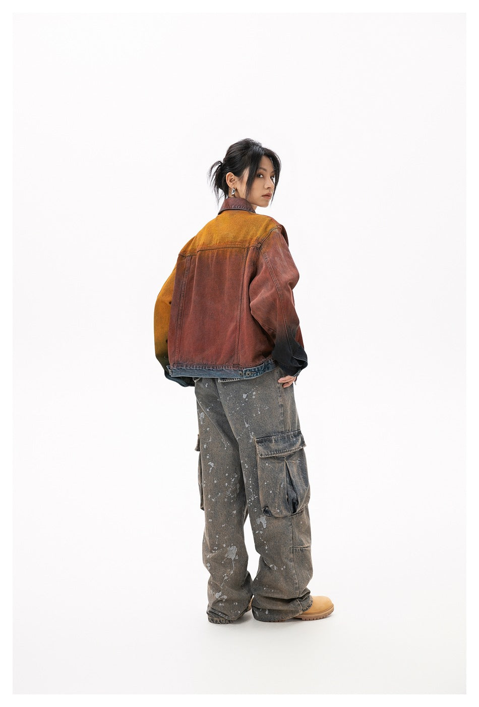 Back view of model in a rust and orange gradient denim-style jacket with blue hem band, worn with cargo jeans