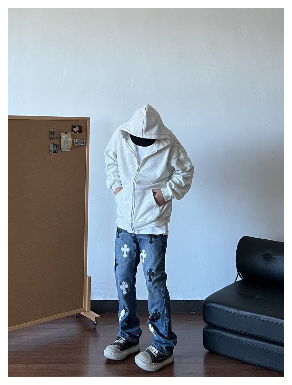 Person wearing a light-gray zip-up hoodie with the hood up, paired with patterned jeans.
