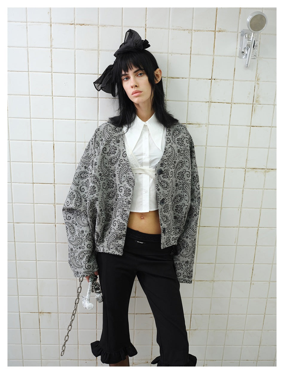 Model wearing a loose gray jacket with black floral paisley print, styled with a white shirt and black trousers.