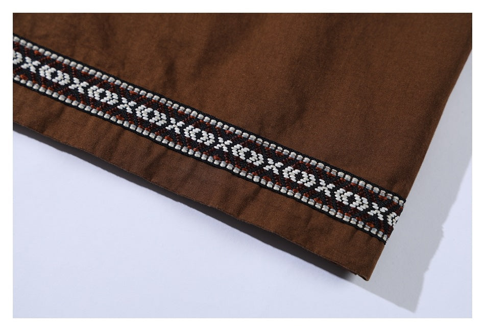 Close-up of the brown shirt hem finished with a black, white, and brown geometric trim band.