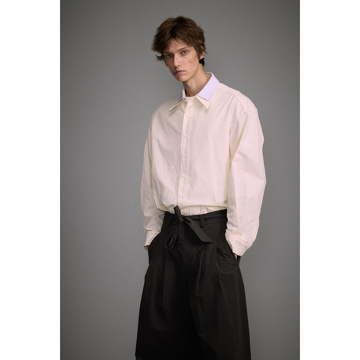 Model wearing an oversized ivory button-up shirt with a pale striped collar and black wide-leg trousers.