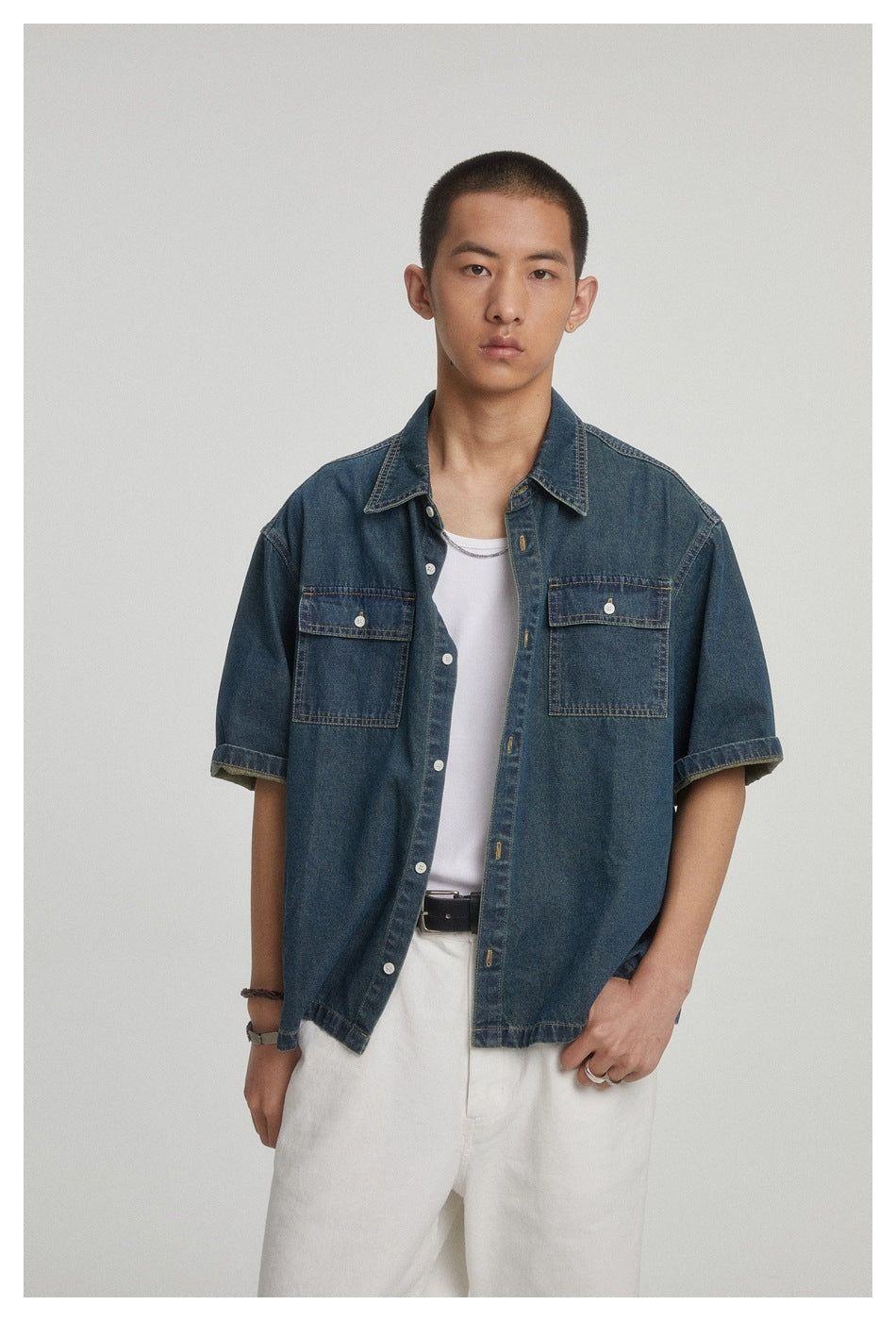 Closer front view of a model wearing a dark blue short-sleeve denim shirt with two button-flap chest pockets.