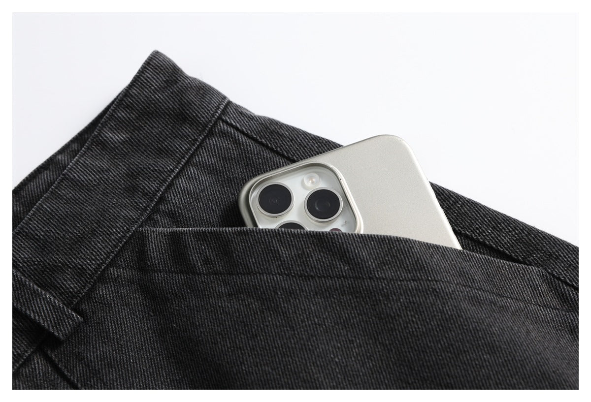 Close-up of a deep pocket in charcoal-black denim trousers holding a silver smartphone.