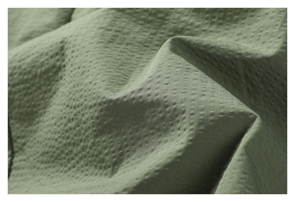 Close-up of sage green fabric with a small raised dotted texture and soft folds.