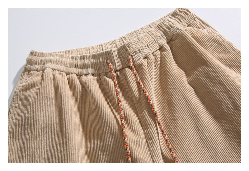 Close-up of beige corduroy shorts showing the gathered elastic waistband and multicolor braided drawstrings.