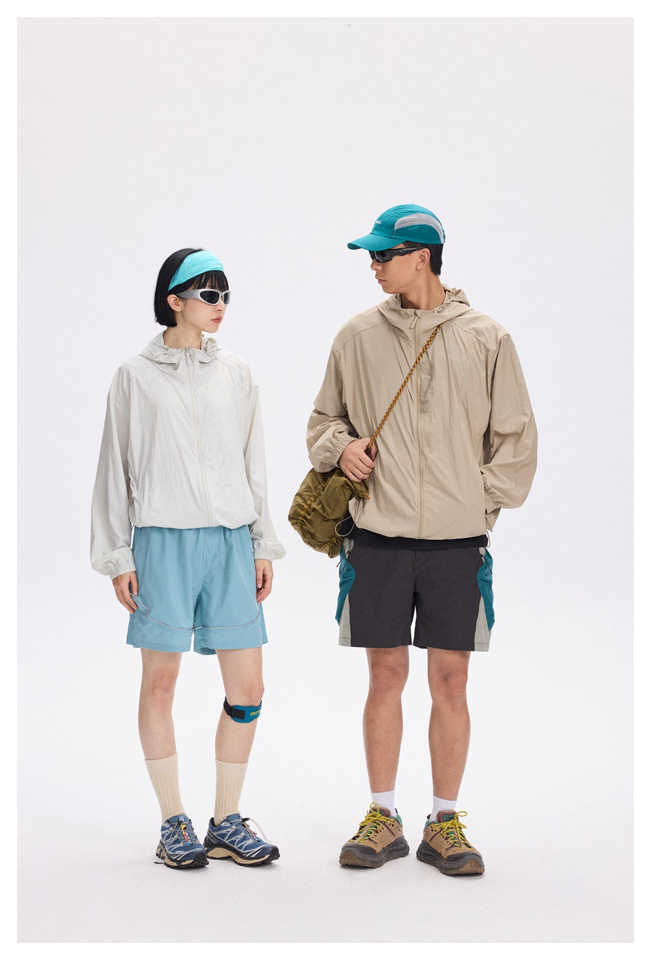 Two models wear hiking outfits, including an off-white jacket with blue shorts and a beige jacket with dark shorts.