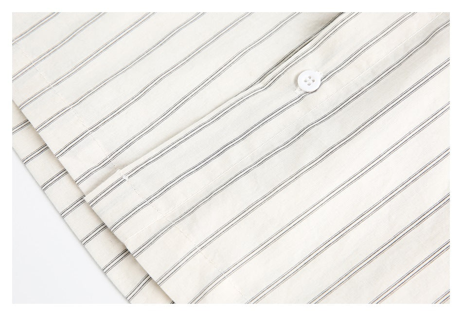 Close-up of the cream shirt's thin dark stripes, a white button, and folded fabric edge.