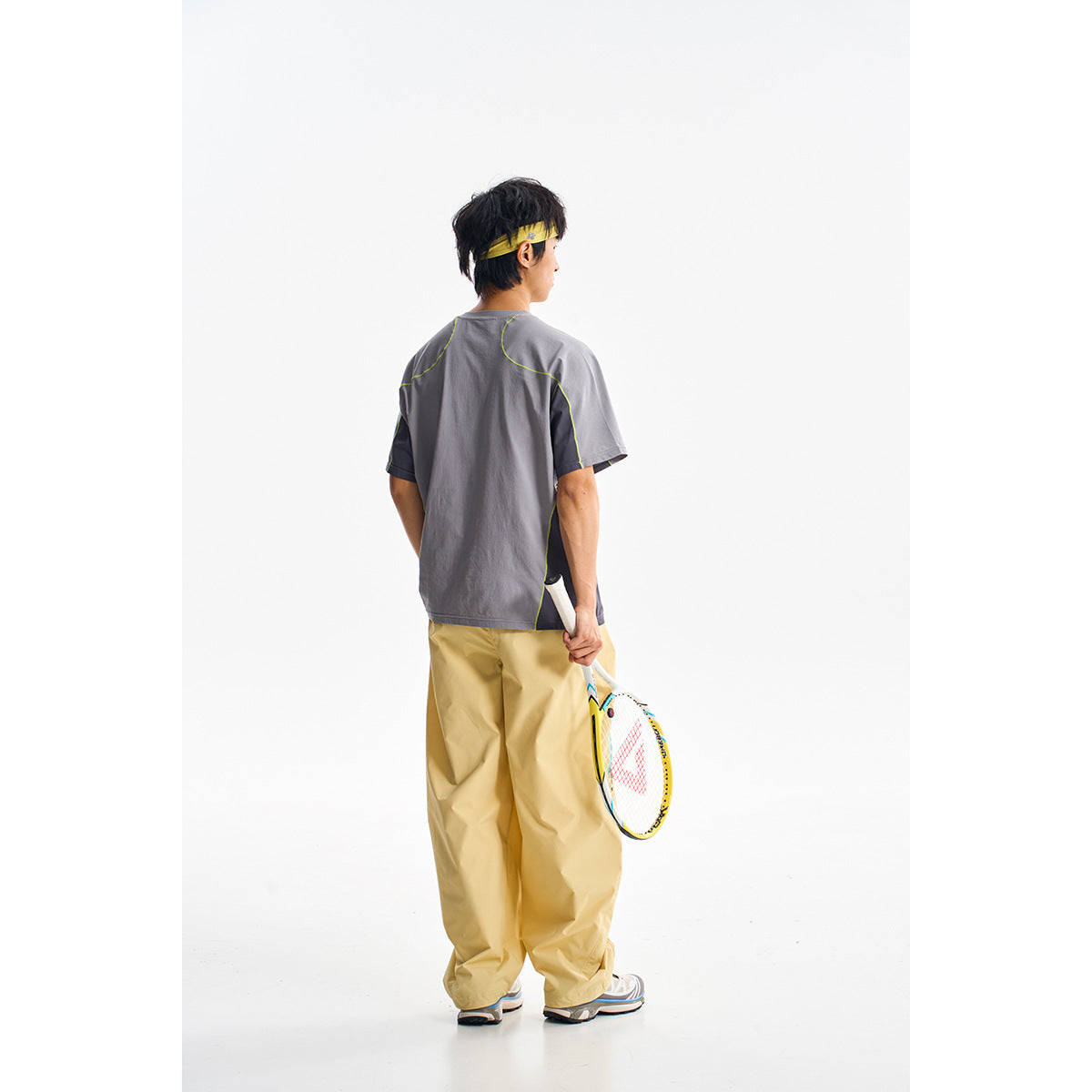 Rear view of a model wearing a gray color-block athletic T-shirt with lime piping and loose tan pants.