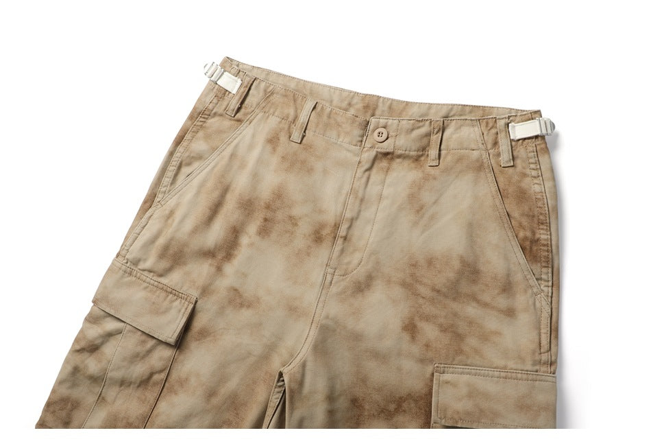 Cropped front view of tan mottled cargo pants with a button waist, side adjusters and large flap pockets.