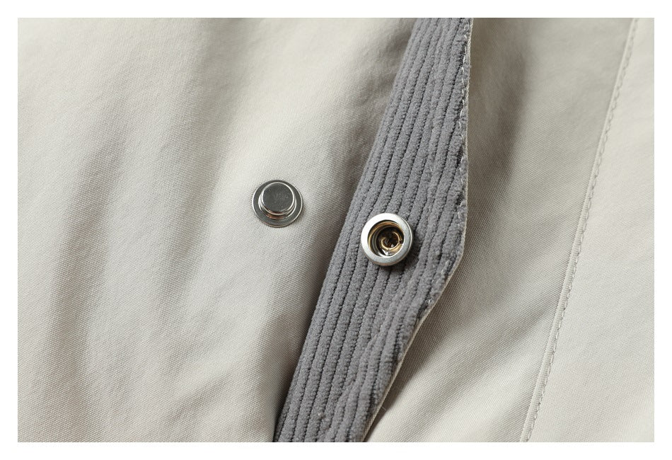 Close-up of a metal snap fastener on a gray ribbed strip against cream coat fabric.